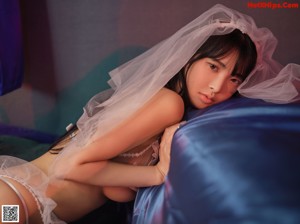 A woman in a wedding dress sitting on a bed.