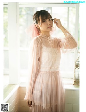 A woman in a pink dress sitting on a window sill.