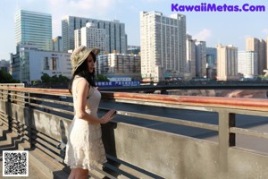 A woman in a white dress and hat standing on a sidewalk.