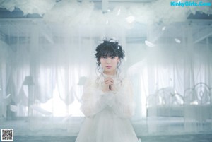 A woman in a white dress standing in front of a window.