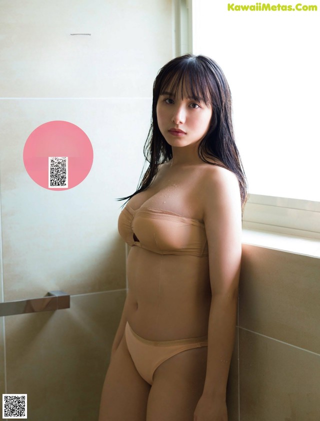 A woman in a nude bodysuit leaning against a window.