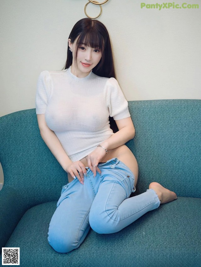 A woman sitting on a blue couch wearing jeans and a white shirt.