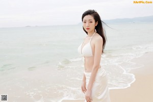 A woman in a white dress sitting on the beach.
