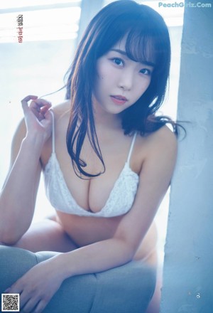 A woman in a white bra and blue shirt laying on a couch.