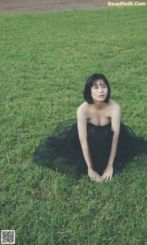 A woman in a black dress standing in the woods.