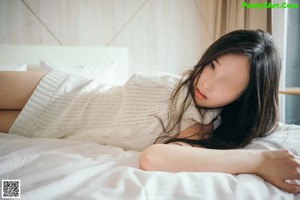 A woman in a white sweater is posing on a bed.