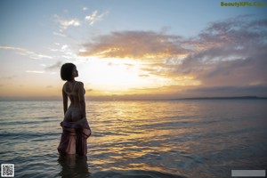 A woman in a pink dress sitting in the water.