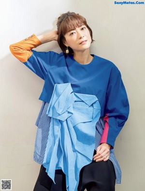 A woman in a blue shirt and black pants posing for a magazine.