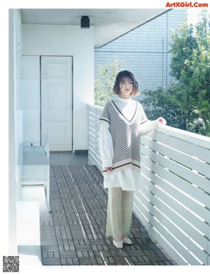 A woman in a white shirt is standing in front of a bush.