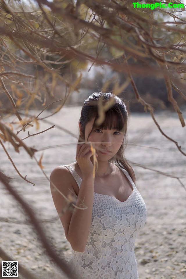 A woman in a white dress standing under a tree.